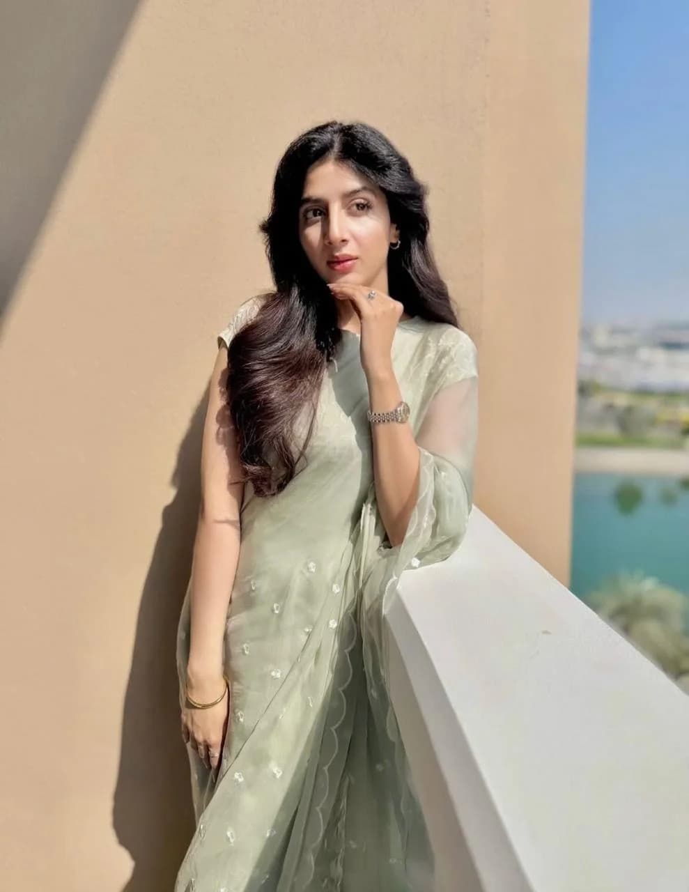 Woman in a mint green embroidered saree posing thoughtfully on a balcony overlooking a waterfront