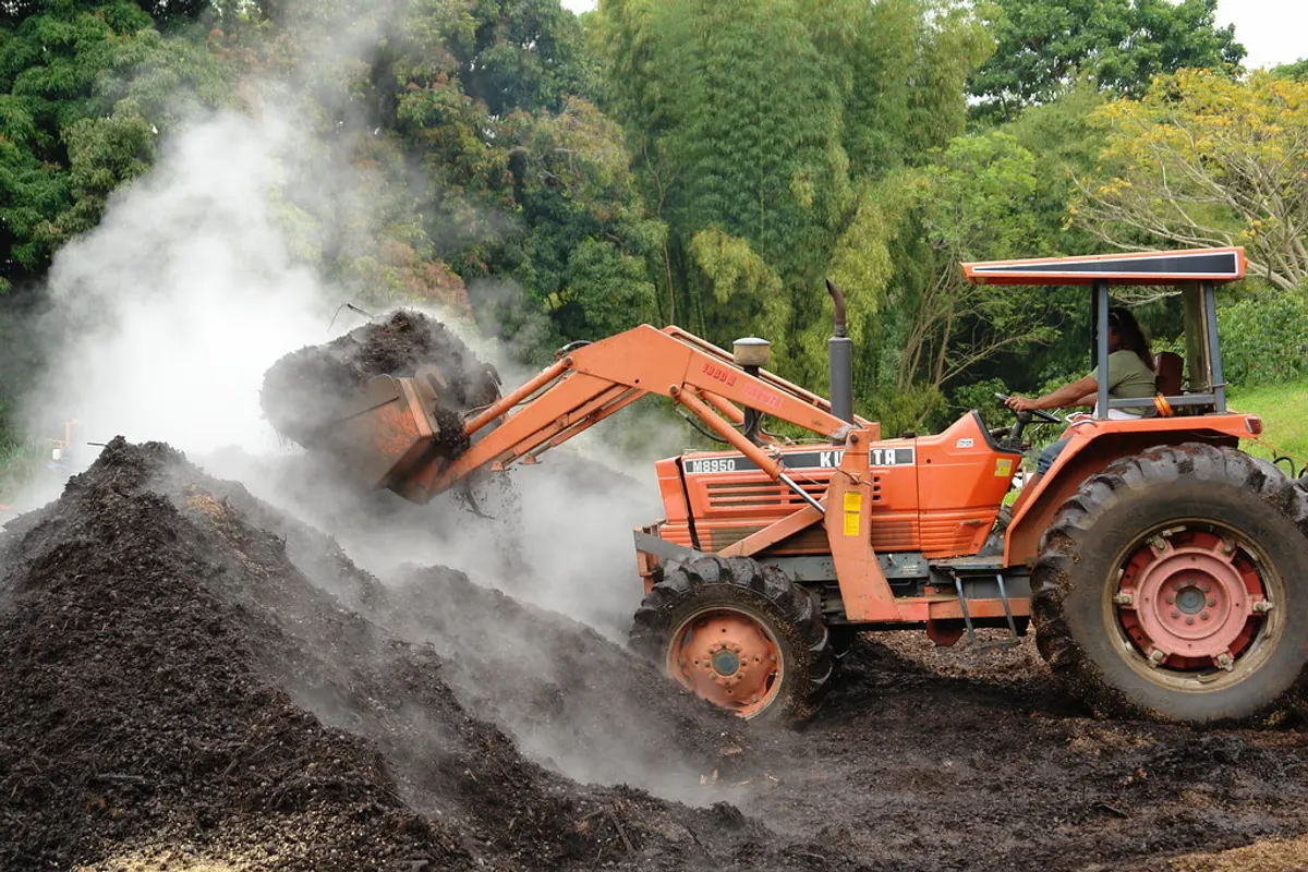 Machine turning a steaming pile of organic waste at a treatment site